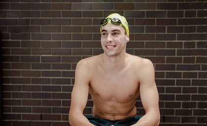 Thomas Neilll sitting with arms on his knees wearing his swimming cap and goggles